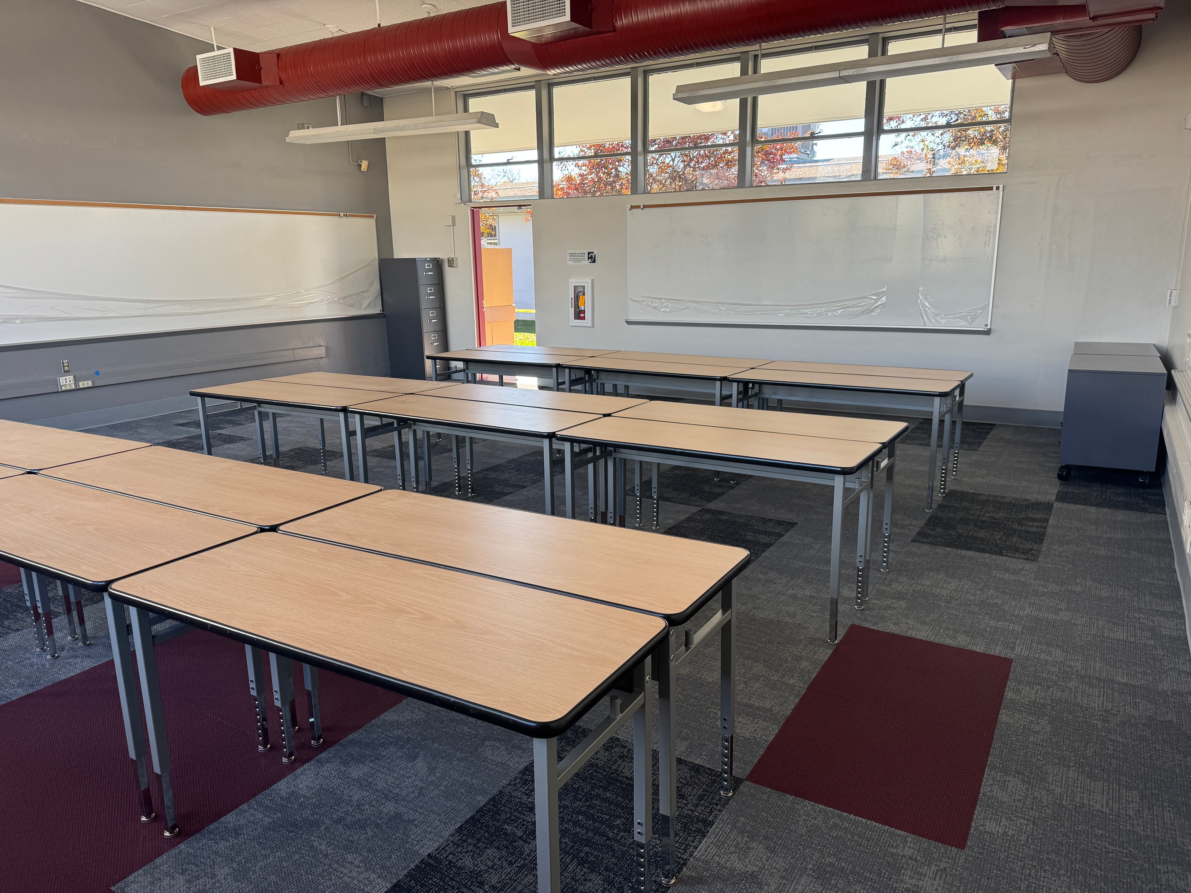 Classroom furniture installation — wood-top tables with red ductwork