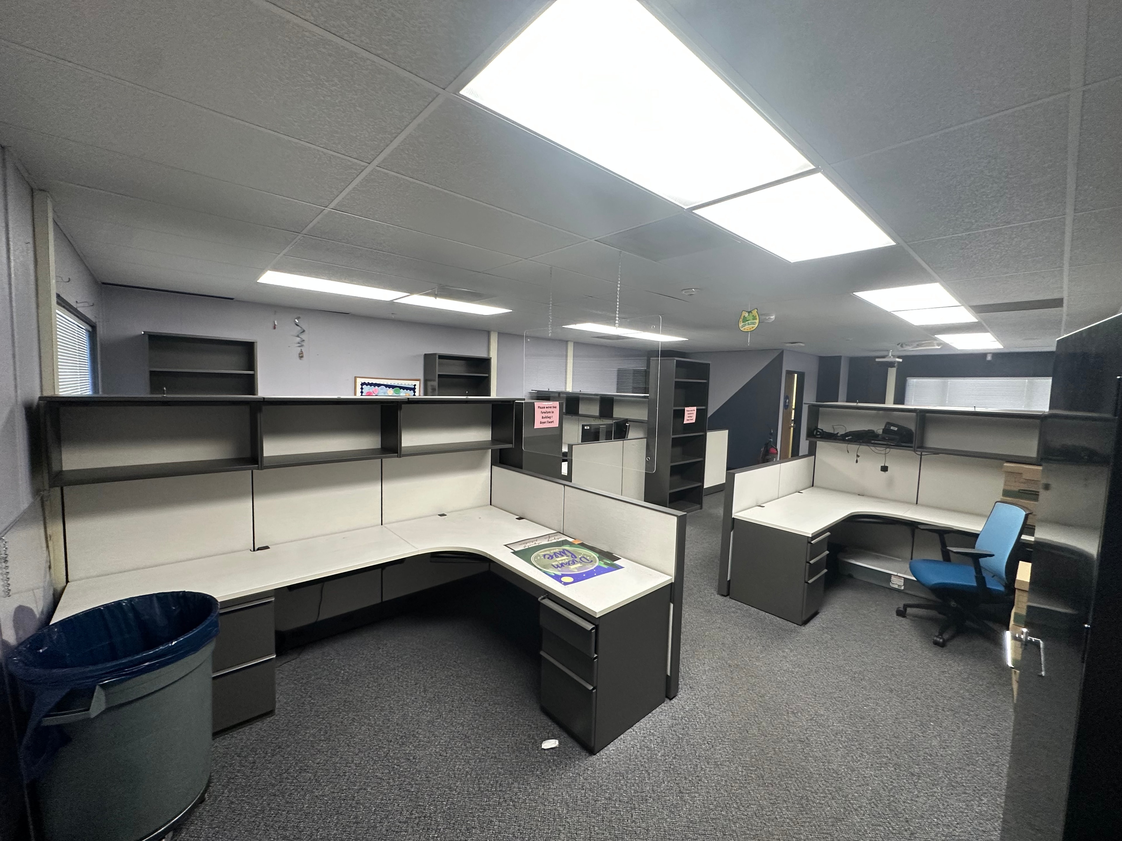 Office cubicle installation with dark charcoal panels and overhead shelving